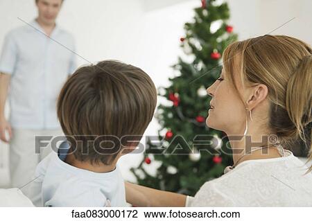 Mother and son sitting in front of Christmas tree, father standing in background View Large Photo Image Stock Image - Mother and son sitting in front of Christmas tree, father standing in background. Fotosearch
