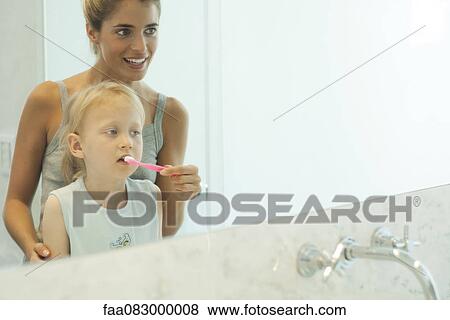 Mother helping daughter brush her teeth View Large Photo Image Stock Photo - Mother helping daughter brush her teeth. Fotosearch