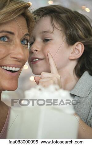 Stock Photography - Mother holding gift, son whispering into ear. Fotosearch