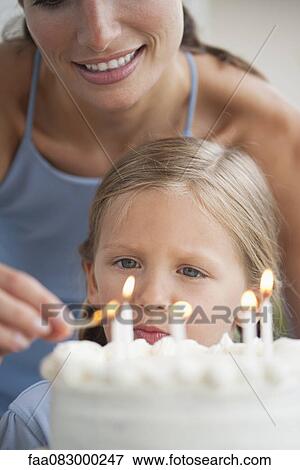 Stock Photo - Mother lighting candles on birthday cake for girl. Fotosearch