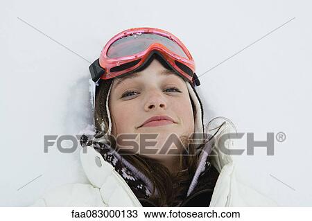 Stock Image - Teenage girl in ski outfit lying in snow. Fotosearch
