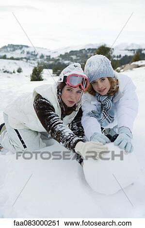 Stock Image - Teenage girls rolling snowball together, portrait. Fotosearch