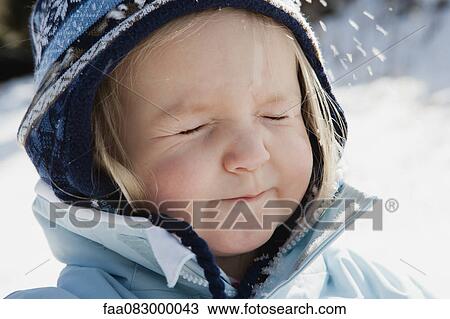 Stock Image - Toddler girl wearing winter clothes in snow with eyes closed, portrait. Fotosearch
