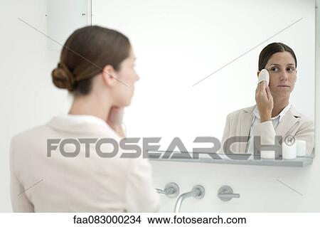 Picture - Woman looking in mirror, putting on make-up with powder puff. Fotosearch