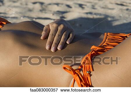 Stock Photo - Woman sunbathing on beach, mid section. Fotosearch