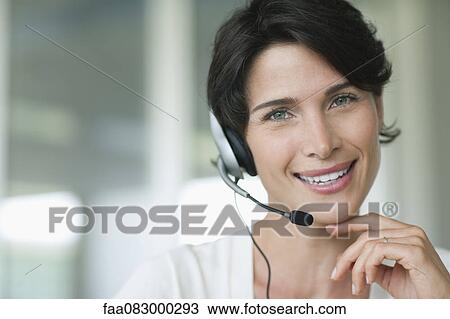 Stock Image - Woman using headset, smiling cheerfully. Fotosearch