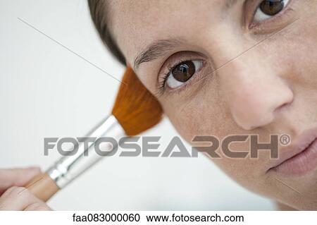 Stock Image - Woman using make-up brush, close-up. Fotosearch