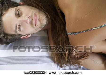 Picture - Young man and girlfriend embracing in bed, directly above. Fotosearch