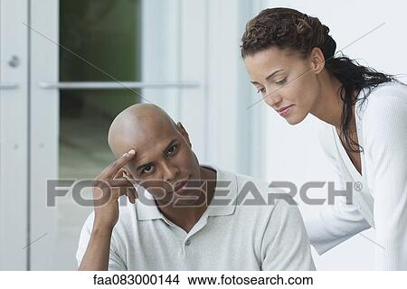 Picture - Young man sitting and looking at camera, young woman leaning towards young man. Fotosearch