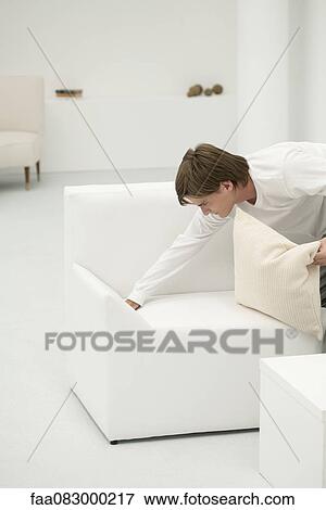 Stock Photo - Young man tidying sofa. Fotosearch