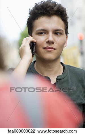 Stock Image - Young man using cell phone outdoors. Fotosearch