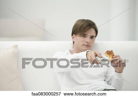 Young man watching TV, changing channel with remote control View Large Photo Image Stock Photo - Young man watching TV, changing channel with remote control. Fotosearch