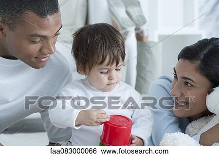 Stock Photograph - Young parents watching baby girl play with toy. Fotosearch