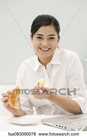 Stock Photo - Young woman eating croissant, smiling. Fotosearch