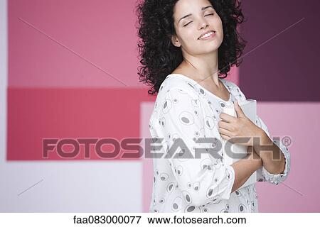 Young woman holding book to chest with eyes closed, smiling View Large Photo Image Stock Photo - Young woman holding book to chest with eyes closed, smiling. Fotosearch