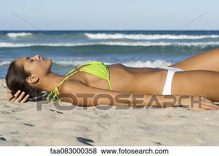 Stock Photo - Young woman in bikini sunbathing on beach. Fotosearch