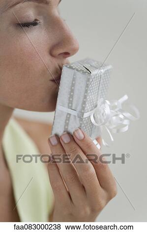 Stock Photo - Young woman kissing gift, eyes closed, side view. Fotosearch
