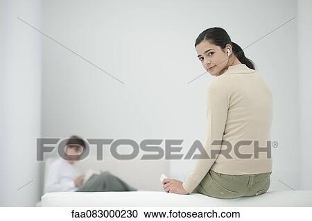 Stock Image - Young woman listening to MP3 player, looking over shoulder. Fotosearch