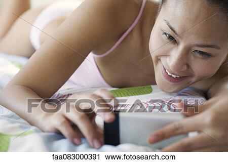Stock Image - Young woman lying down in underwear, looking at cell phone. Fotosearch