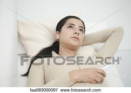 Young woman lying on sofa, listening to MP3 player View Large Photo Image Stock Photo - Young woman lying on sofa, listening to MP3 player. Fotosearch