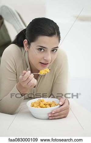 Stock Photo - Young woman lying on stomach, eating bowl of cereal. Fotosearch