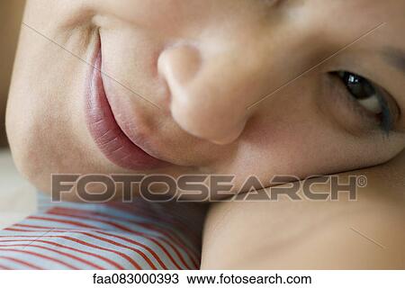 Stock Image - Young woman resting head on arm, smiling, close-up. Fotosearch