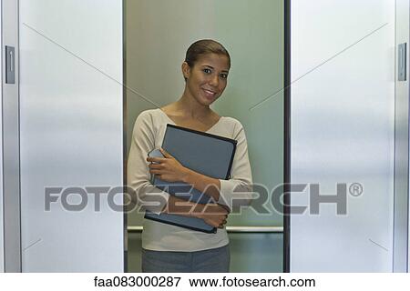 Stock Photo - Young woman standing in elevator, doors closing. Fotosearch