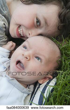 Stock Photo - Boy lying on grass with baby brother, portrait. Fotosearch