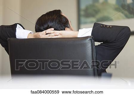 Stock Photo - Business executive relaxing in office chair with hands behind head. Fotosearch