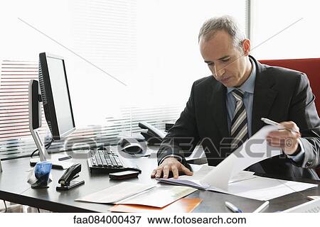 Business executive reviewing documents in office View Large Photo Image Stock Photo - Business executive reviewing documents in office. Fotosearch