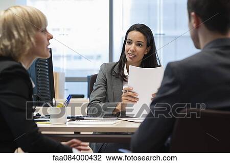 Stock Image - Business partners in meeting, focus on businesswoman in background. Fotosearch