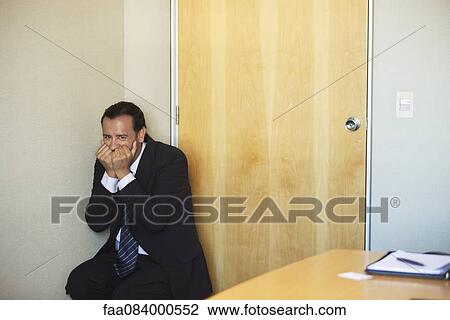 Stock Image - Businessman crouching in corner with terrified expression. Fotosearch