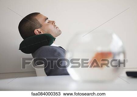 Businessman resting with neck pillow in office, side view View Large Photo Image Stock Image - Businessman resting with neck pillow in office, side view. Fotosearch