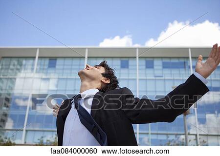 Stock Image - Businessman standing in front of building with arms outstretched. Fotosearch