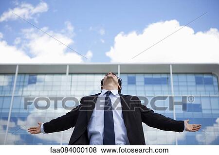 Stock Photo - Businessman standing in front of building with arms outstretched. Fotosearch