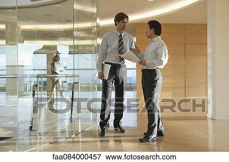 Businessmen discussing document in office corridor View Large Photo Image Stock Photo - Businessmen discussing document in office corridor. Fotosearch