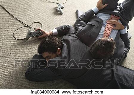 Picture - Businessmen sleeping on carpet floor by video game controllers. Fotosearch