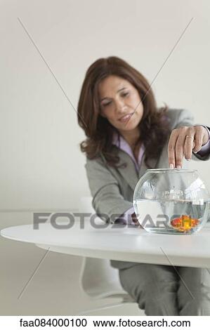 Stock Image - Businesswoman feeding goldfish. Fotosearch