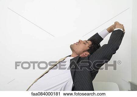 Stock Image - Exhausted mid-adult businessman stretching with eyes closed. Fotosearch