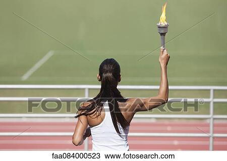 Female athlete holding up flaming torch, rear view View Large Photo Image Stock Image - Female athlete holding up flaming torch, rear view. Fotosearch