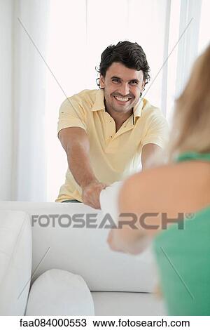 Stock Image - Man and woman playing tug-of-war with sofa cushion. Fotosearch
