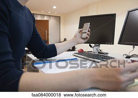 Man working at desk in office, holding cell phone, mid section View Large Photo Image Stock Photo - Man working at desk in office, holding cell phone, mid section. Fotosearch