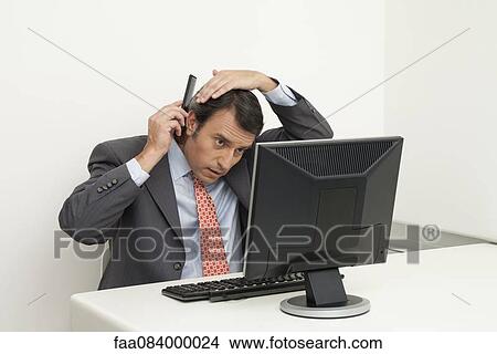 Picture - Mature businessman combing hair at desk. Fotosearch