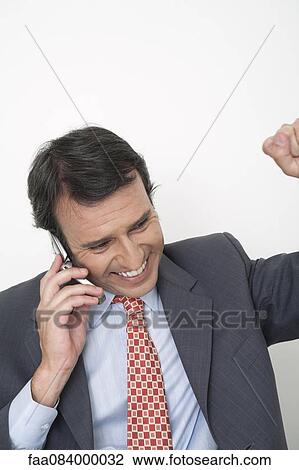 Stock Image - Mature businessman punching fist while using cell phone. Fotosearch