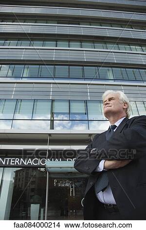 Mature businessman standing in front of office building with arms folded View Large Photo Image Picture - Mature businessman standing in front of office building with arms folded. Fotosearch