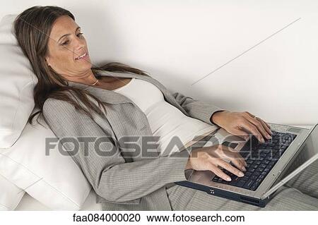 Mature businesswoman lying on couch typing on laptop computer View Large Photo Image Stock Image - Mature businesswoman lying on couch typing on laptop computer. Fotosearch