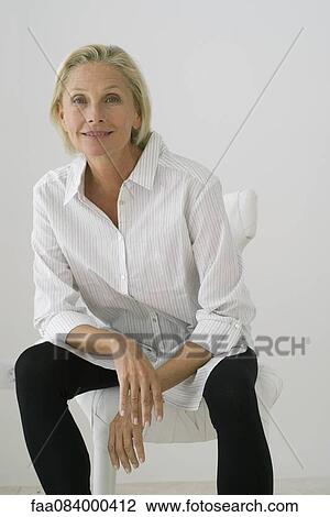 Stock Image - Mature woman sitting in chair, portrait. Fotosearch