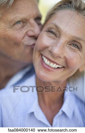 Stock Image - Mature woman smiling as man kisses her cheek, portrait. Fotosearch