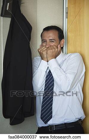 Stock Photo - Mid-adult businessman in corner covering mouth with hands. Fotosearch