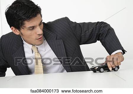 Stock Image - Mid-adult businessman playing with toy car. Fotosearch